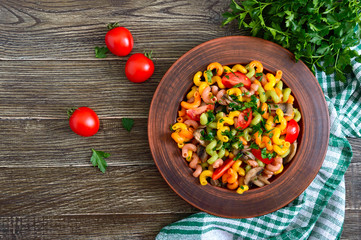 Tasty warm salad. Colored pasta with mushrooms and fresh tomatoes in a bowl on a wooden table. Pasta colorata. The top view