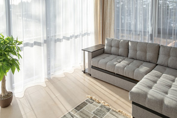 Modern interior with big sofa and a large windows. Morning sunlight from the windows