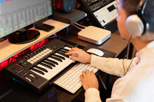 Asian Man Learning Online Music Production Technology On Computer And Midi Keyboard From Internet In Home Studio