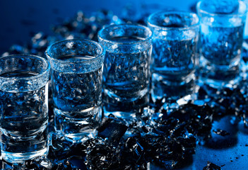 Damp glasses of vodka with ice on a black reflective background.