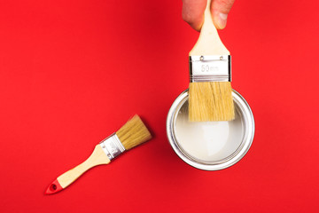 hand holding Brush  on open can of   paint on red  background. Renovation concept - Image