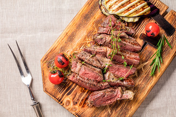 Juicy medium rare beef steak slices on wooden board with herbs spices and salt.