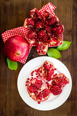 Juicy pomegranate with seeds on plate on dark wooden table top-down
