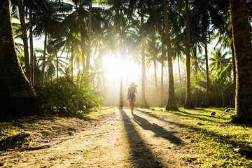 A beautiful  girl wearing a large hat and a red bikini is walking on a path surrounded by coconut...