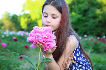 Fototapeta premium Flowering peonies. Beautiful Caucasian girl with long brunette hair in a botanical garden where bright pink and white peonies bloom. Nature and relaxation. Botanical Garden. Flowers