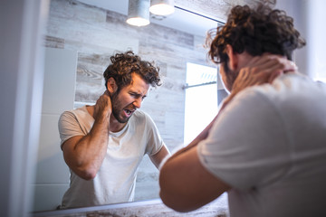 Obraz premium Portrait of sleepy young man yawning and looking at mirror in bathroom in morning, side view. Trying to wake up. Lack of sleep, insomnia and stressful lifestyle. Hangover. depression.