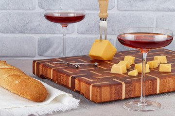 Two elegant glasses of red wine on a thin stem, sliced cheese and bread on a cutting Board with a beautiful pattern, standing on the kitchen table. Mediterranean snacks and wines.