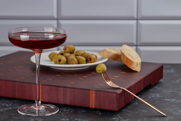Elegant glass of red wine on a thin stem, an olive on a fork, and a plate of pitted olives on a...