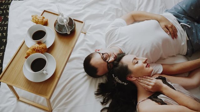 Couple in a bedroom lying together, hugging with closed eyes, tender and cute. Touching moment of happy relationship. Continental breakfast in morning in bed, in a hotel, apartment. Two lovers lay.