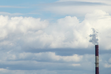 Smoke from a red-and-white pipe of a thermal power plant against a background of white clouds and...