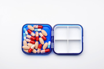 many tablets and capsules in a plastic container on a white background.