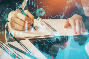 Forex chart hologram on hand taking notes background. Concept of analysis. Multi exposure