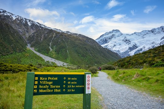 A sign to the kea point is a walking path to view the Muller Glacier and Muller Lakes in Mount Cook National Park. Rocky mountains and green grass in summer season in New Zealand.