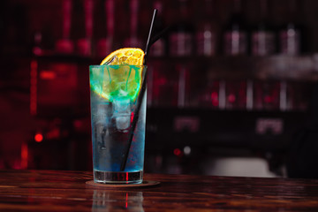 blue syrup cocktail with a slice of dried orange stands at the bar