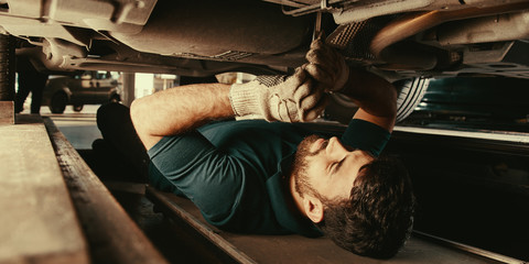 Mechanic under car during repair in workshop - obrazy, fototapety, plakaty