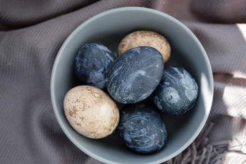 Easter background with Easter eggs and feathers in a ceramic gray bowl. Background with easter eggs. Naturally dyed eggs prepared for Easter on gray texture tablecloth background. Happy Easter