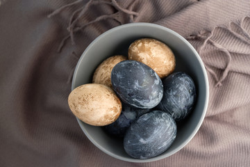 Easter background with Easter eggs and feathers in a ceramic gray bowl. Background with easter eggs. Naturally dyed eggs prepared for Easter on gray texture tablecloth background. Happy Easter