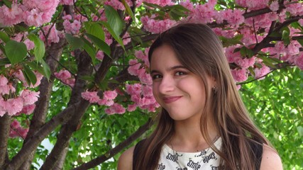 Fototapeta premium Young girl with beautiful make-up stands under a tree with bright pink sakura flowers