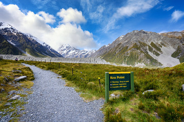 Signs and paths to view points at the Kea Point Track in Mount Cook National Park, high rocky mountains and green grass in summer in New Zealand.