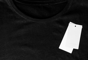 Black t-shirt close-up and white clean label top view. Textile background, t-shirt with tag.