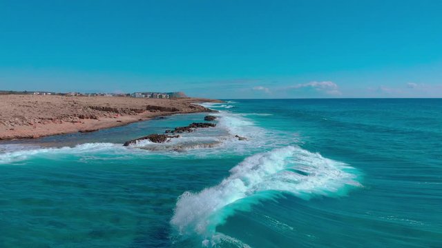 Cyprus Aya Napa, flight over the sea seashore, aerial drone view of waves crashing at rocky cliff with splashing and white foam, view of stones in blue water