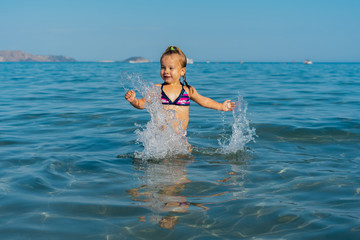 a little girl enthusiastically jumps into the sea and laughs, splashes fly around her. summer...