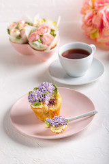 Flower cupcakes and cup of tea on white background. Beautiful sponge cup cakes decorated with buttercream lilac flower.