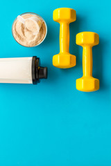 Sport nutrition. Whey protein, shaker, dumbbells on blue background top-down flay lay copy space