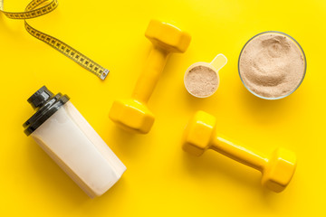 Sport nutrition. Whey protein, shaker, dumbbells on yellow background top-down flay lay
