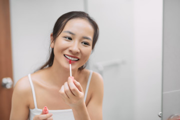 Beautiful Asian woman looking mirror and apply lip make up lipstick in powder room bathroom toilet