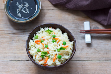 Vegetarian rice dish with vegetables and green peas on a wooden background.