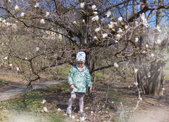  A little girl sits on the steps in the spring botanical garden where the magnolia blossomed