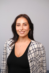 Portrait of a smiling mid-aged business woman with dark hair and brown eyes in glasses in jacket against a light wall