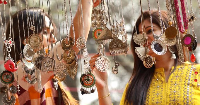 Two women shopping for necklace and earrings at street market