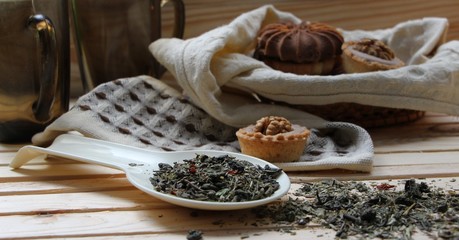 green tea with herbs on a white spoon on a background of a basket with homemade cookies and mugs