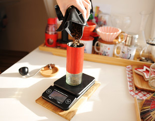 Alternative brewing. Pouring coffee beans into red manual coffee grinder on scale. Third wave specialty aesthetics