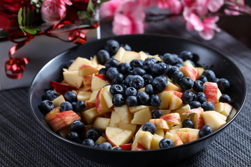 Fruit salad on a dark plate with red roses bouquet on the background