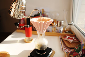 Alternative manual coffee brewing. Pouring water from gooseneck kettle into pink ceramic origami dripper