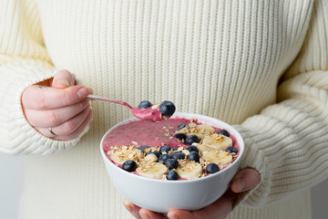 Berry smoothie bowl in hands of female wearing white sweater. 