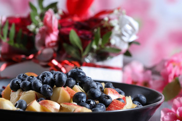 Fruit salad on a dark plate with red roses bouquet on the background
