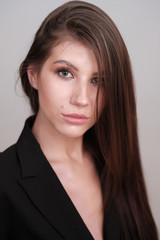 Fototapeta premium Close-up portrait of a beautiful cute girl with long hair and in a black jacket on a light background. Girl posing for the photographer in a photo studio.