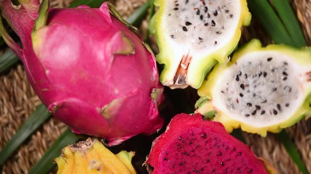 Yellow and pink pitahaya on palm branch, rotating background. Top view. Citrus fruits. Vegan and raw food concept. Sliced dragon fruit texture