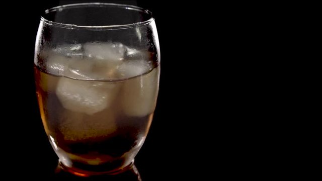 Close-up. Ice cubes rotating and melts in a glass of whiskey. Isolated on white background. Rotating ice bubes in  whiskey on black background.