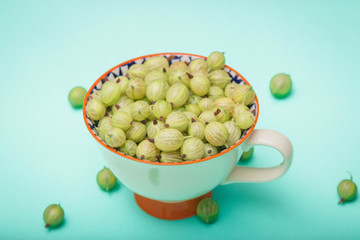 Fresh gooseberries in glass bowl on turquoise stone slate background. Top view.