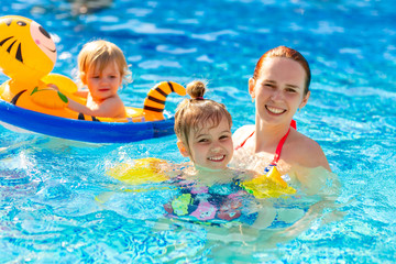 mum and two daughter play in the pool. rubber ring