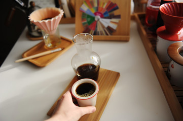 Black filter coffee in ceramic cup in hand. Bamboo board. Glass decanter. Third wave specialty aesthetics