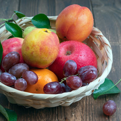 red grape berries and fresh fruits in a straw basket on a dark wooden background.