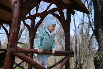  Little girl plays in a wooden gazebo in a spring botanical garden where primroses bloom