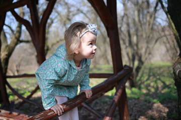  Little girl plays in a wooden gazebo in a spring botanical garden where primroses bloom