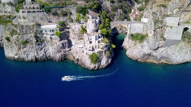 Fiordo di Furore arch bridge with car traffic passing above and a boat exiting the fjord, Amalfi coast in Salerno Italy, Aerial drone pan-left rotating shot